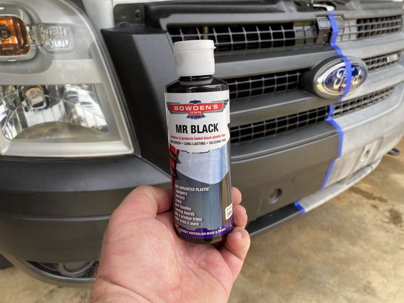 Hand holding car detailing product in front of a vehicle grille and headlight.