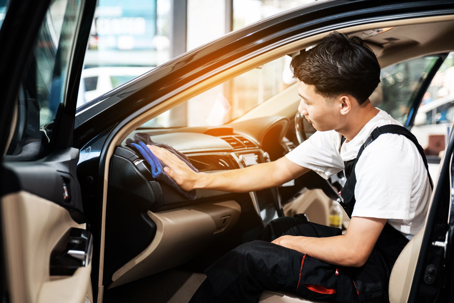 A man cleaning the interior car console with a dry blue microfiber towel, car detailing (or valeting) concept. Automobile professional cleaning service. Selective focus.