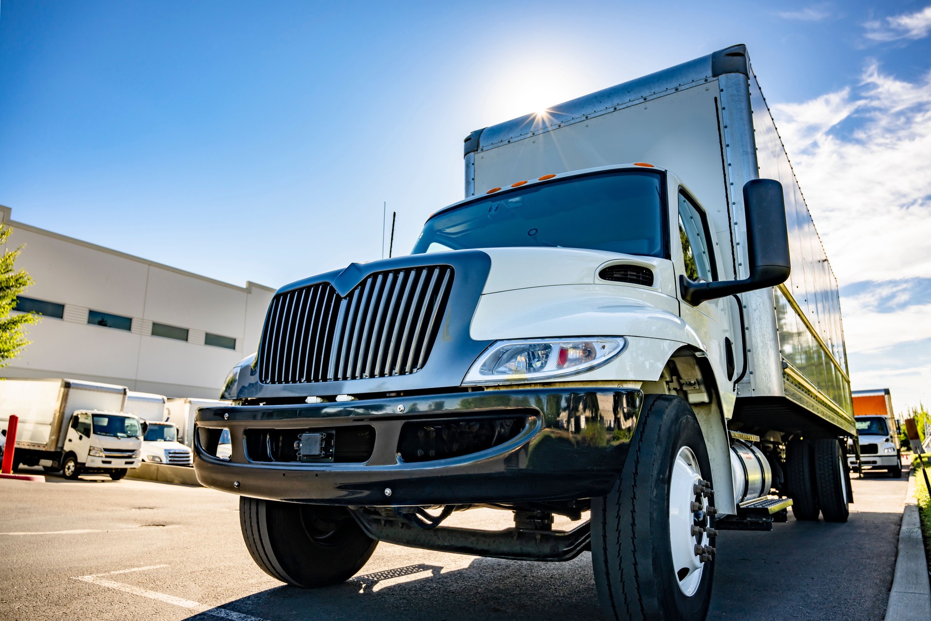 Compact middle duty rig semi truck with long box trailer standing on the wide warehouse parking lot with another trucks